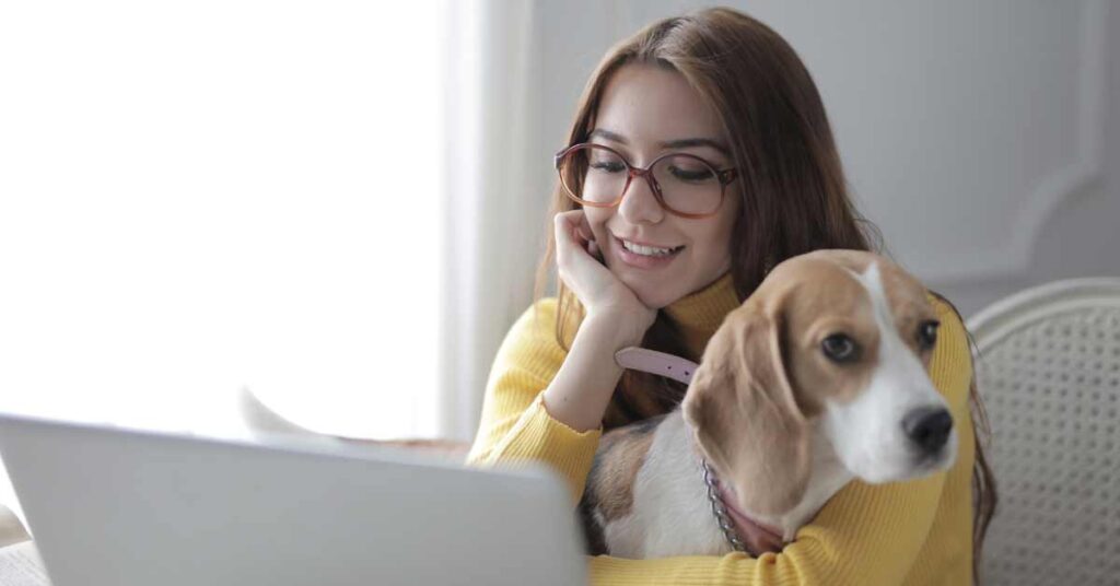 Image of a happy woman sitting with her dog in front of a laptop