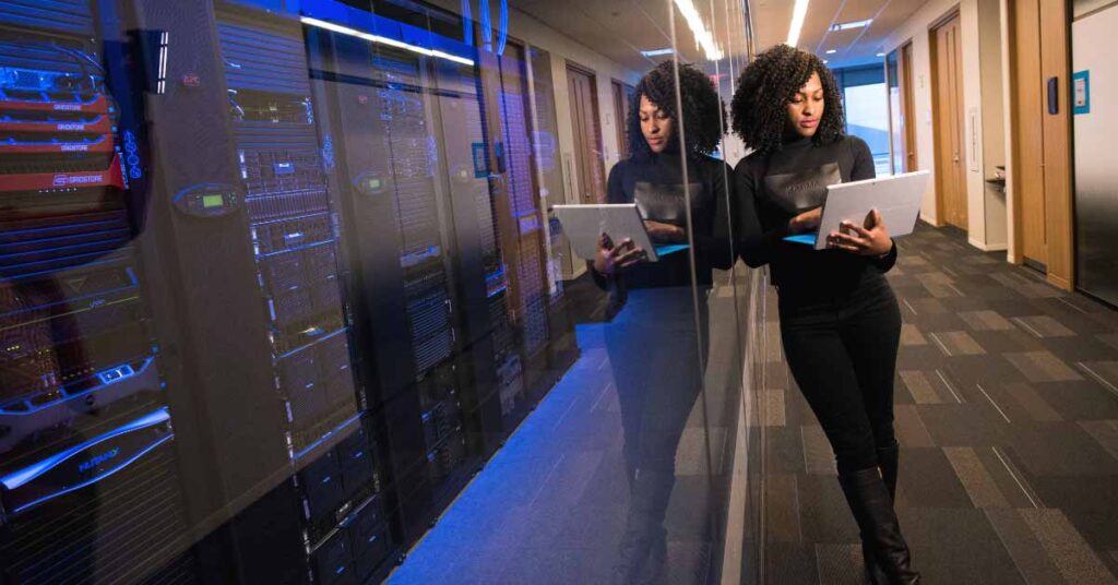 Woman standing with laptop while leaning against server room